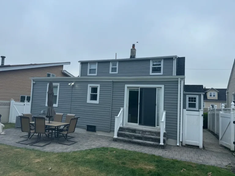 Back of a house with new gray vinyl siding, a patio and a sliding door
